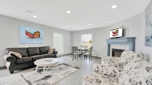 A living room with a sofa, a coffee table, a fireplace, and a dining area with chairs. - Schmidt's Creek Hotel (Osage Beach)