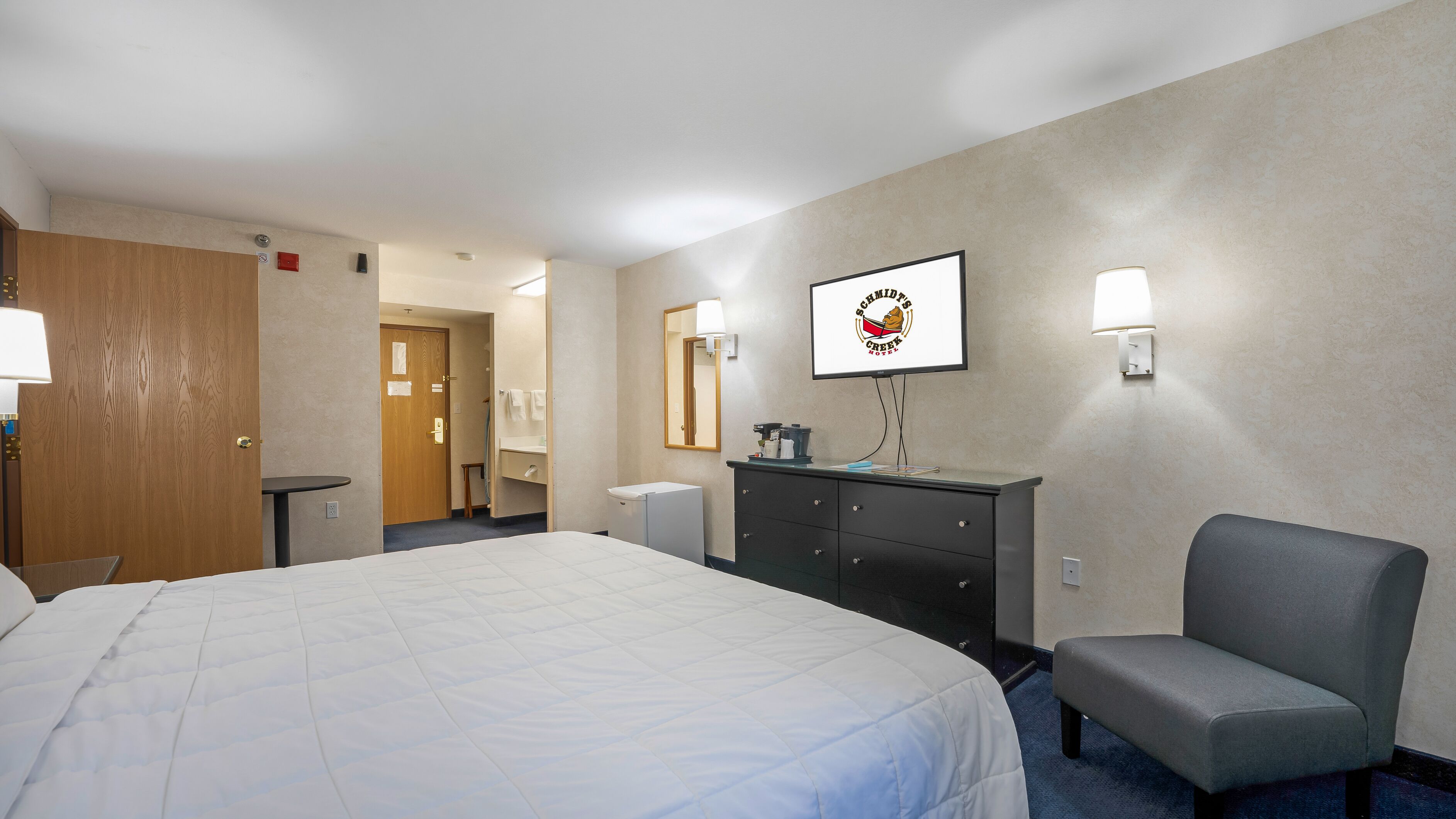 A hotel room with a large bed, a desk, a chair, a dresser, and a mirror.
