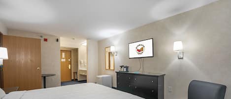 A hotel room with a large bed, a desk, a chair, a dresser, and a mirror.