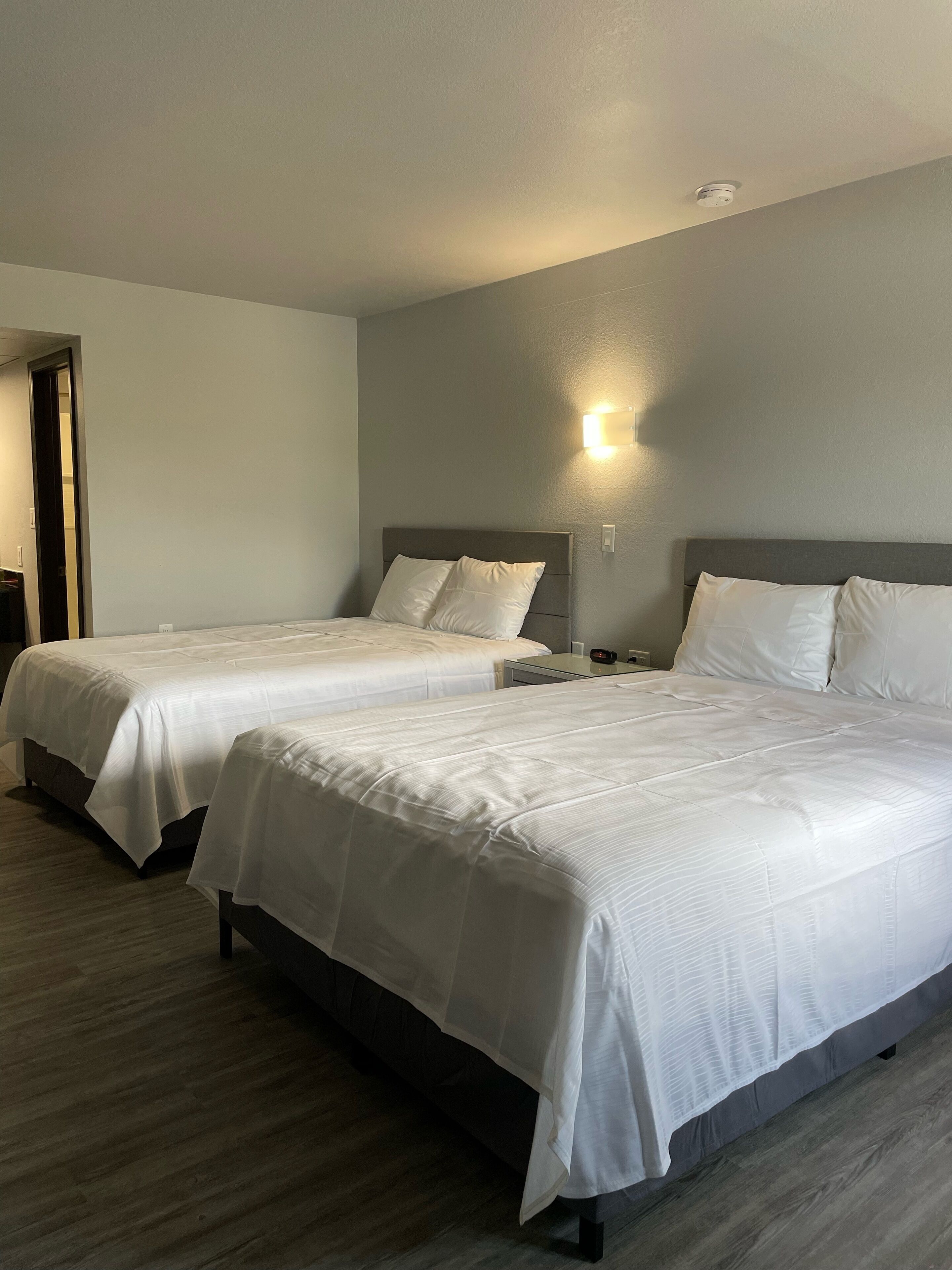 Une chambre d’hôtel avec deux lits, une table de chevet, une lampe fixée au mur et une porte.