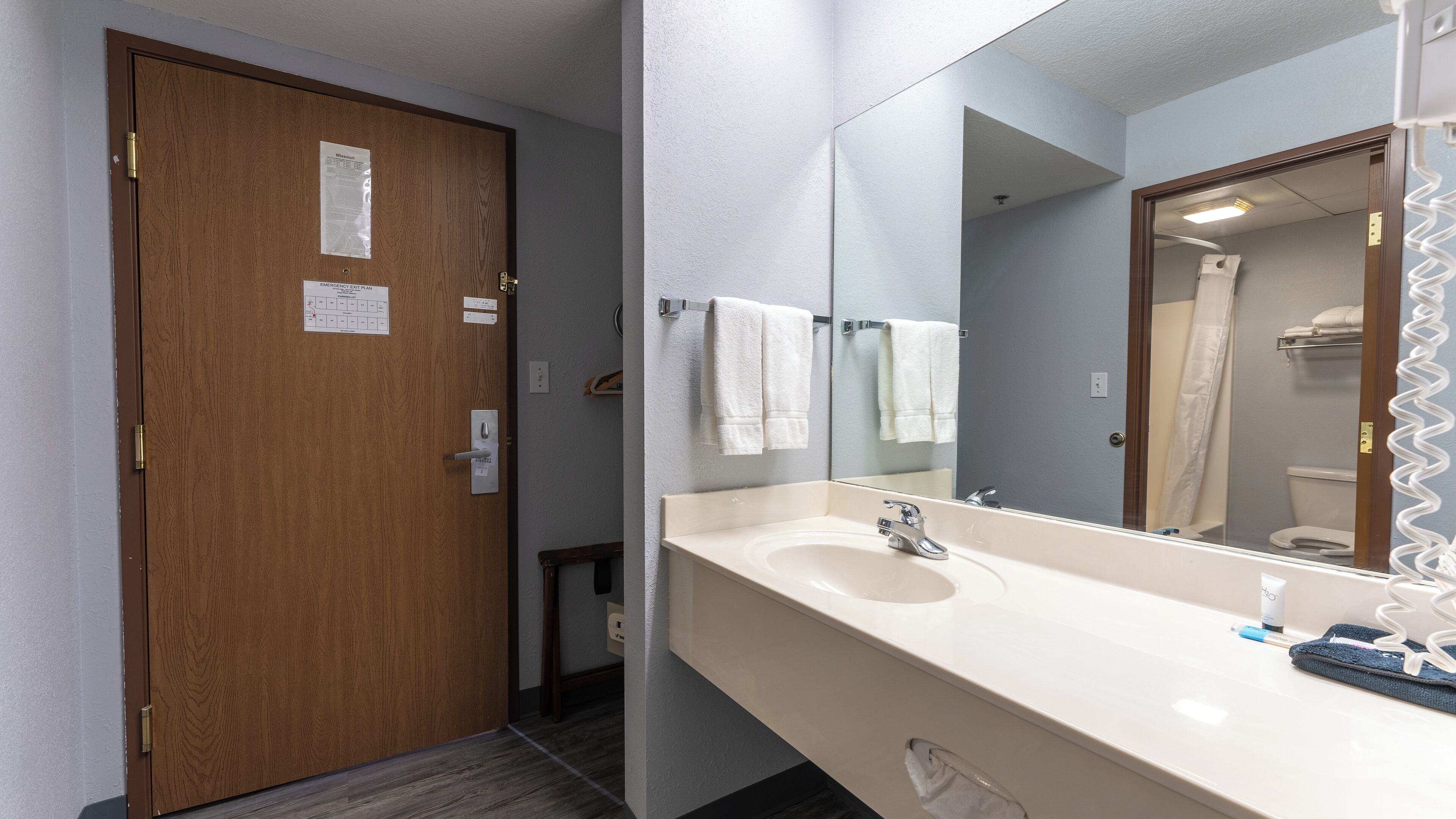 Un baño con puerta de madera, un lavabo con espejo y un perchero para toallas.