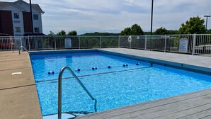 A rectangular swimming pool with clear blue water, surrounded by a wooden deck and metal fencing. - Schmidt's Creek Hotel (Osage Beach)