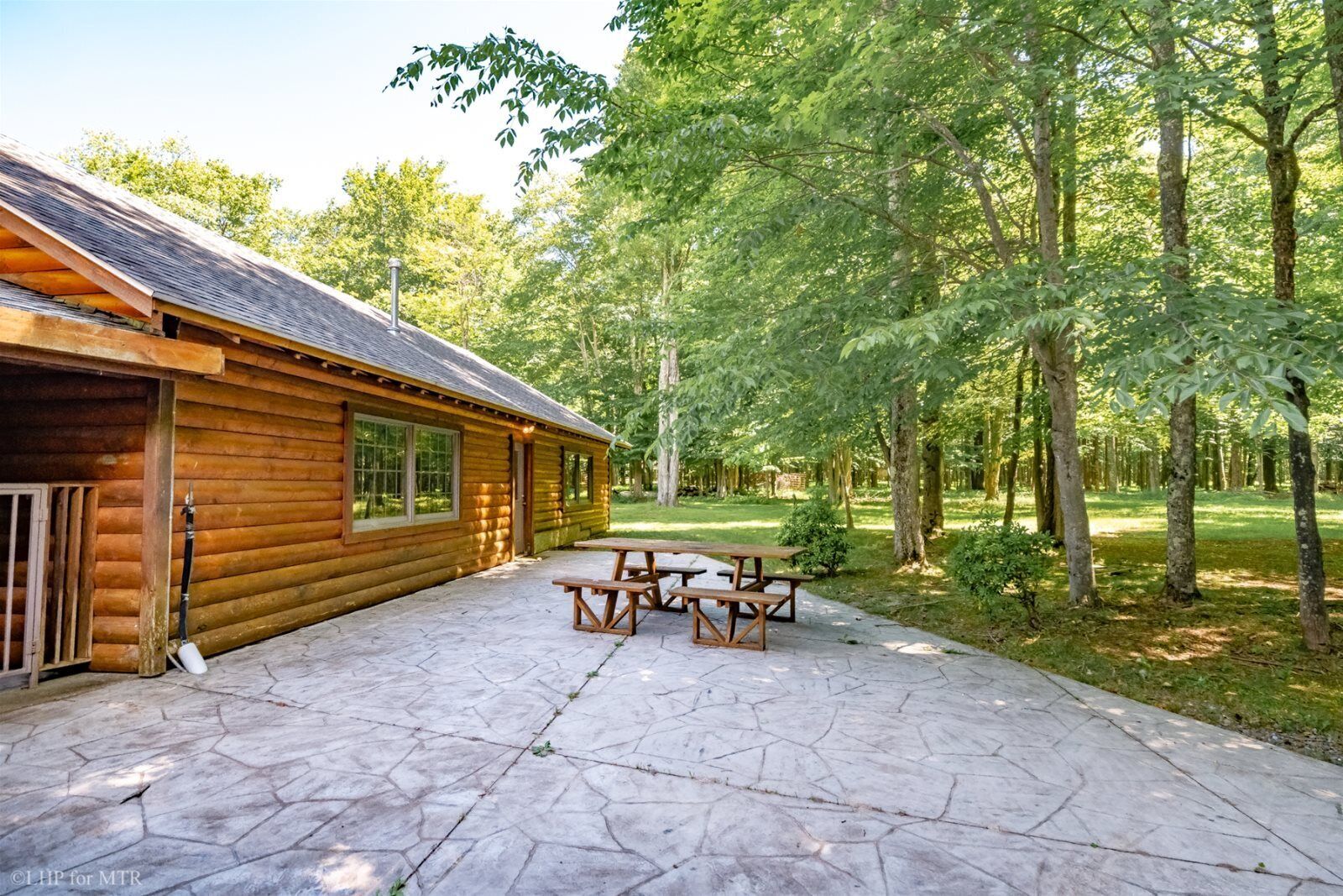 A log cabin with a stone patio and picnic tables.