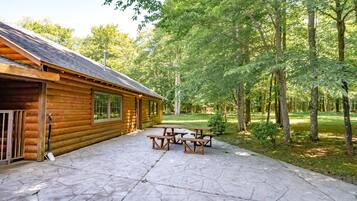 A log cabin with a stone patio and picnic tables.