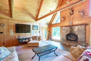 A cozy cabin interior with a stone fireplace, wooden walls, a flat-screen TV, and a comfortable seating area.