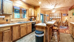 A wooden cabin kitchen with a central island, wooden cabinets, and a dining area with chairs.