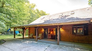 A log cabin with a covered patio area, stone flooring, and a small outdoor seating area with chairs.
