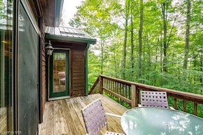 A wooden deck with a glass door leading to a small room, surrounded by a forest. - Tucked Inn (Davis)