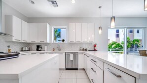 Une cuisine moderne avec des meubles blancs, un îlot central et une vue sur un balcon agrémenté de plantes.