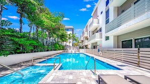 Une piscine dotée d’une terrasse carrelée, entourée d’une végétation luxuriante et de bâtiments modernes.