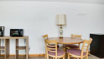 Un comedor con una mesa redonda de madera, cuatro sillas de madera con cojines morados, una lámpara, un microondas y un refrigerador negro.