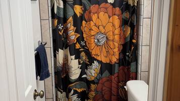 A bathroom with a toilet, a shower curtain with floral patterns, and a blue towel hanging on the door.