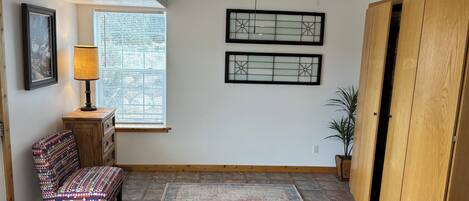 A room with a ceiling fan, a patterned rug, a bench, a window with blinds, and a wooden door.