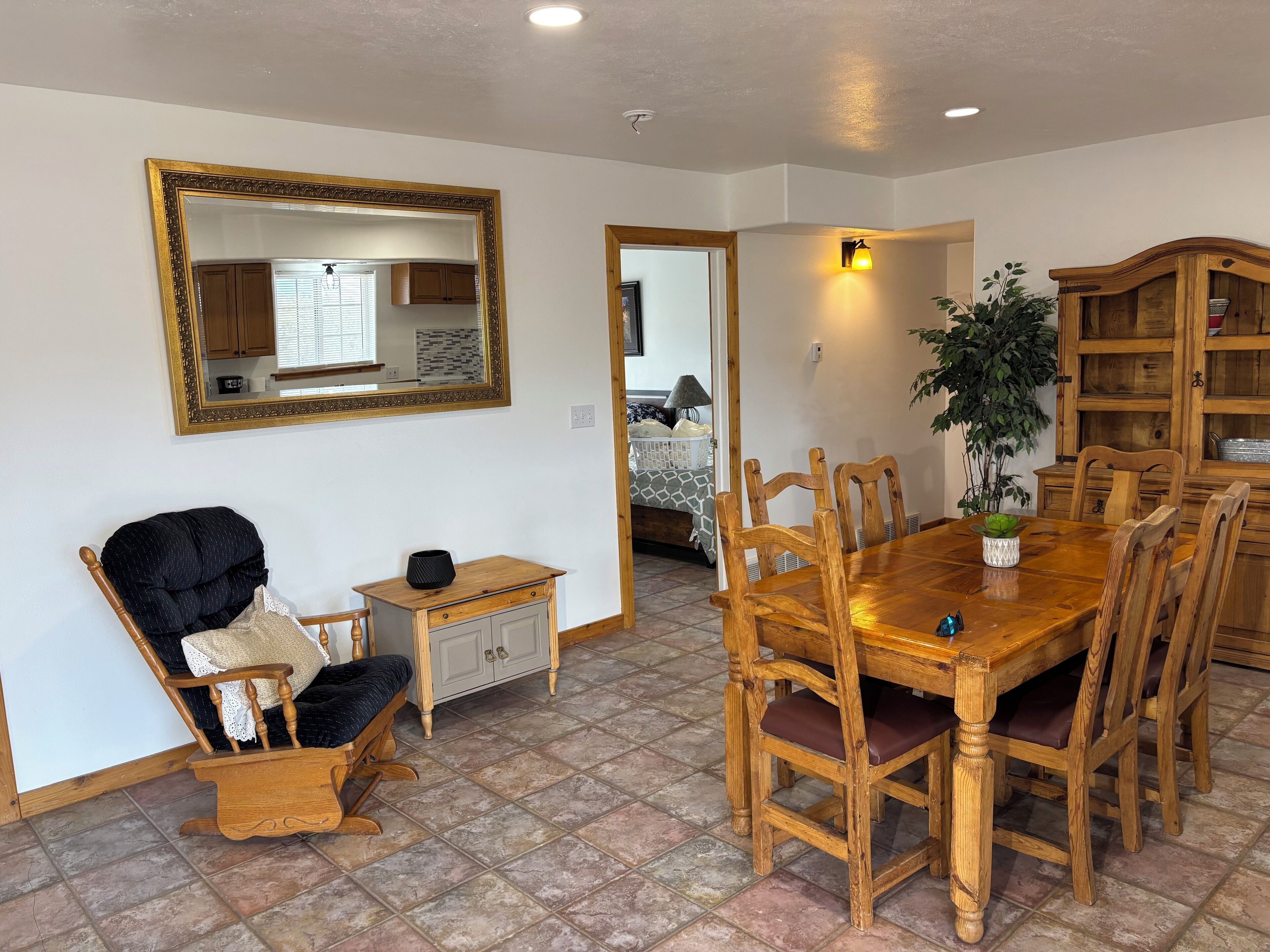 A dining area with a wooden table and chairs, a mirror on the wall, and a small cabinet.