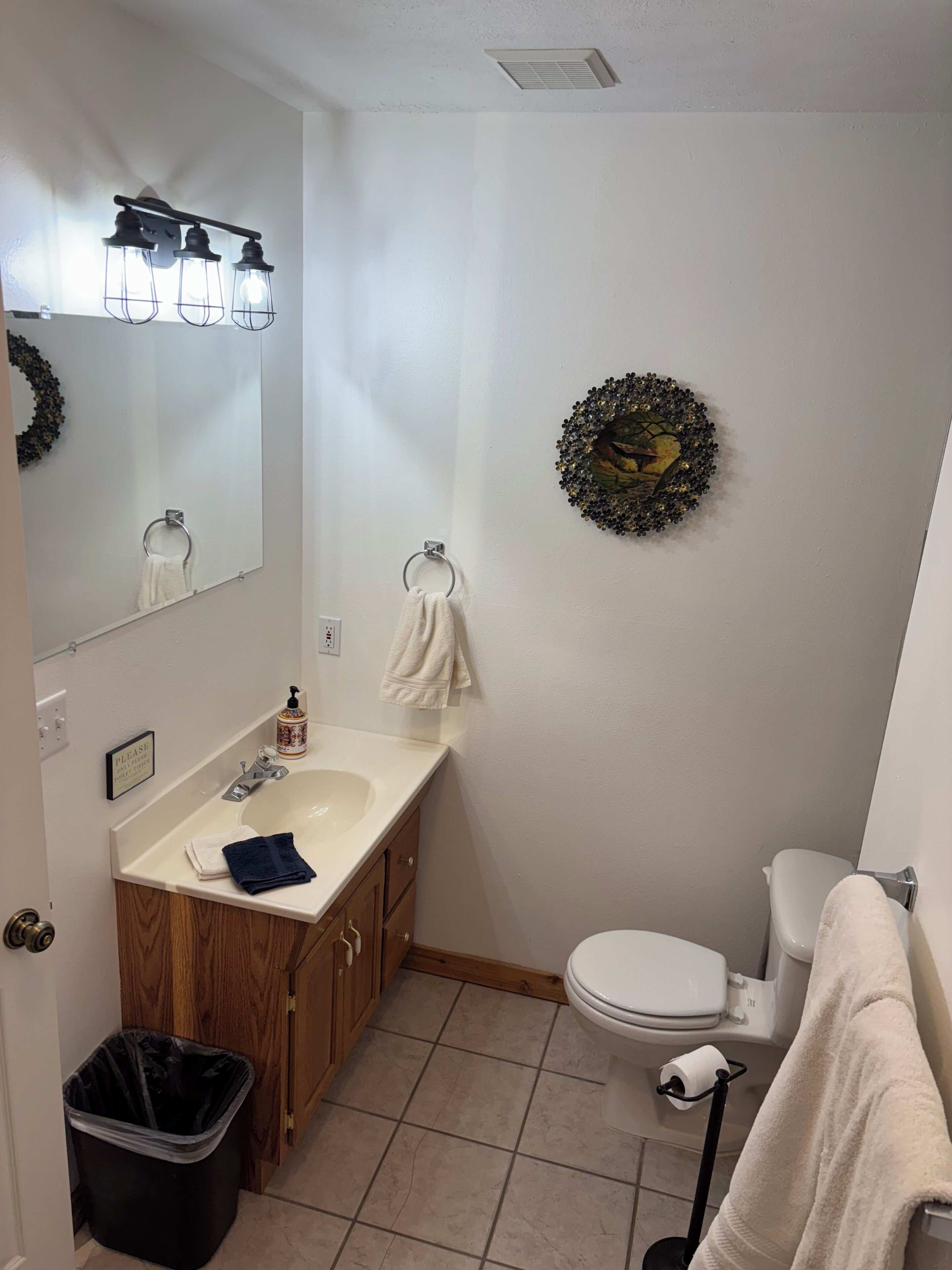 A bathroom with a sink, mirror, toilet, and a trash bin.