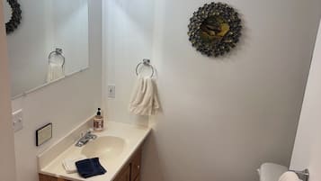 A bathroom with a sink, mirror, toilet, and a trash bin.