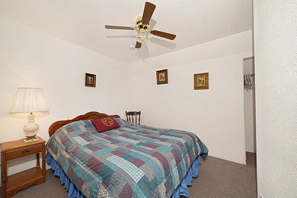 Une chambre à coucher comprenant un lit, une table de chevet, une chaise, un ventilateur de plafond et trois tableaux encadrés accrochés au mur.
