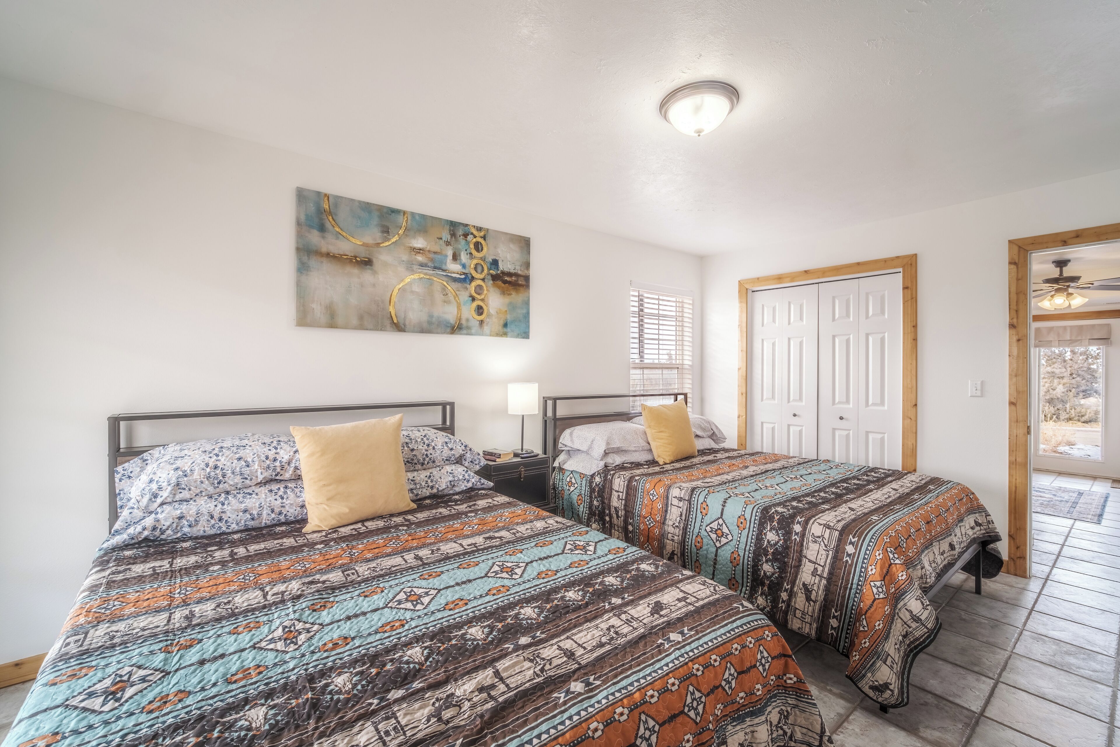 Habitación con dos camas, cada una con ropa de cama estampada, una lámpara en el techo y una puerta con marco de madera.