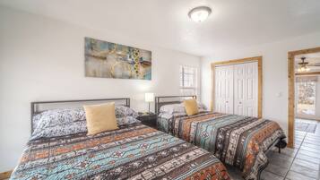 Habitación con dos camas, cada una con ropa de cama estampada, una lámpara en el techo y una puerta con marco de madera.