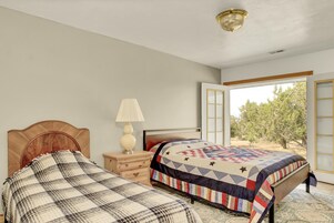 A bedroom with two beds, a nightstand, a lamp, and a view of the outdoors.