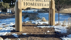 A wooden sign with the text "Wind Walker Homestead" in a rural setting with snow on the ground and trees in the background. - Ranchette Ponderosa - The La Sal #4 at Wind Walker Homestead (Spring City)