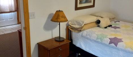 Une chambre à coucher comprenant un lit, une table de chevet, une lampe, une porte et un tableau accroché au mur.