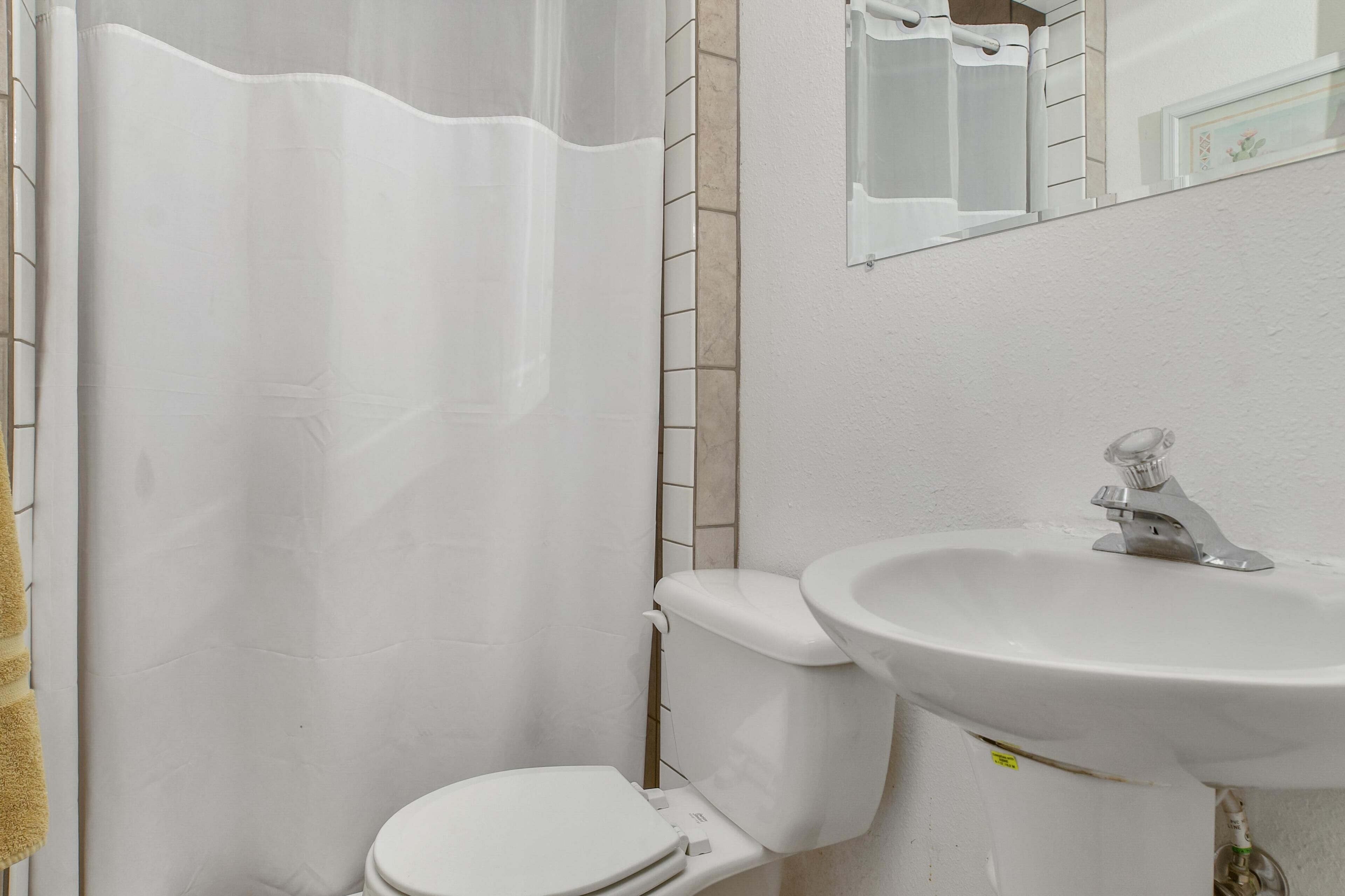 Un baño con inodoro blanco, lavamanos y cortina de ducha.