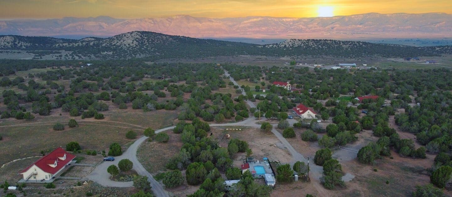 An aerial view of a rural area with scattered houses, a swimming pool, and a mountainous backdrop.