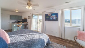 A bedroom with a large bed, a small kitchenette, a TV on the wall, and a balcony with a view. - The Harmony Studio at Wind Walker Homestead (Spring City)