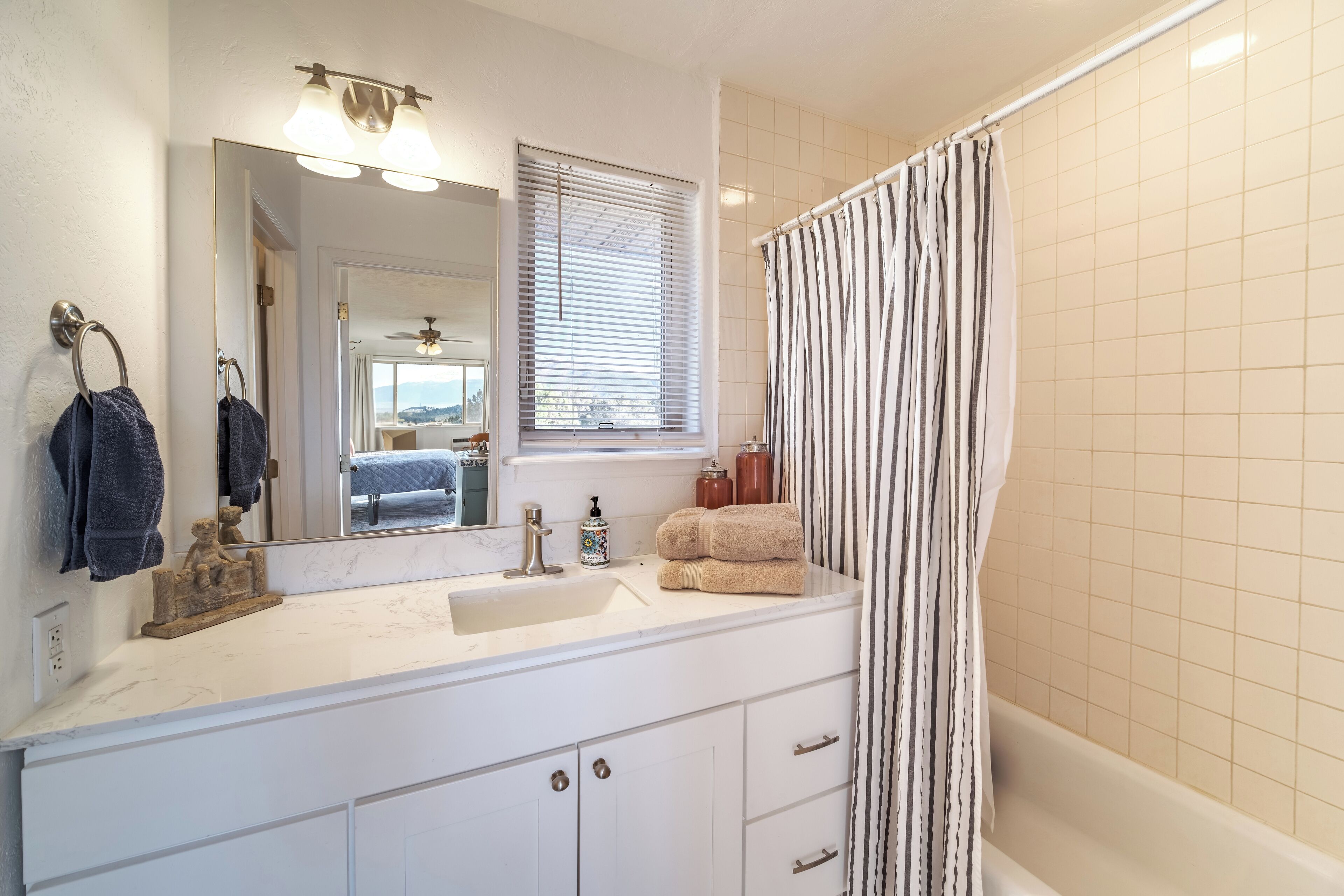 A bathroom with a white sink, a mirror, a window with blinds, a shower curtain, and a bathtub.