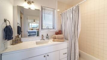 A bathroom with a white sink, a mirror, a window with blinds, a shower curtain, and a bathtub.