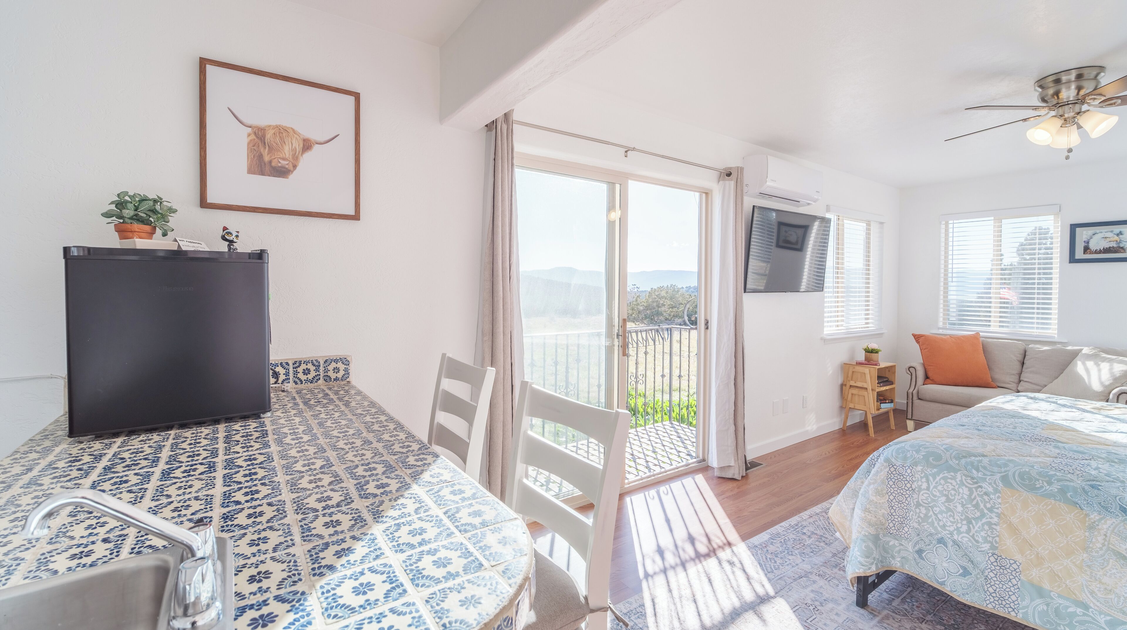 Un dormitorio con cama, escritorio, silla, televisor y balcón con vistas.