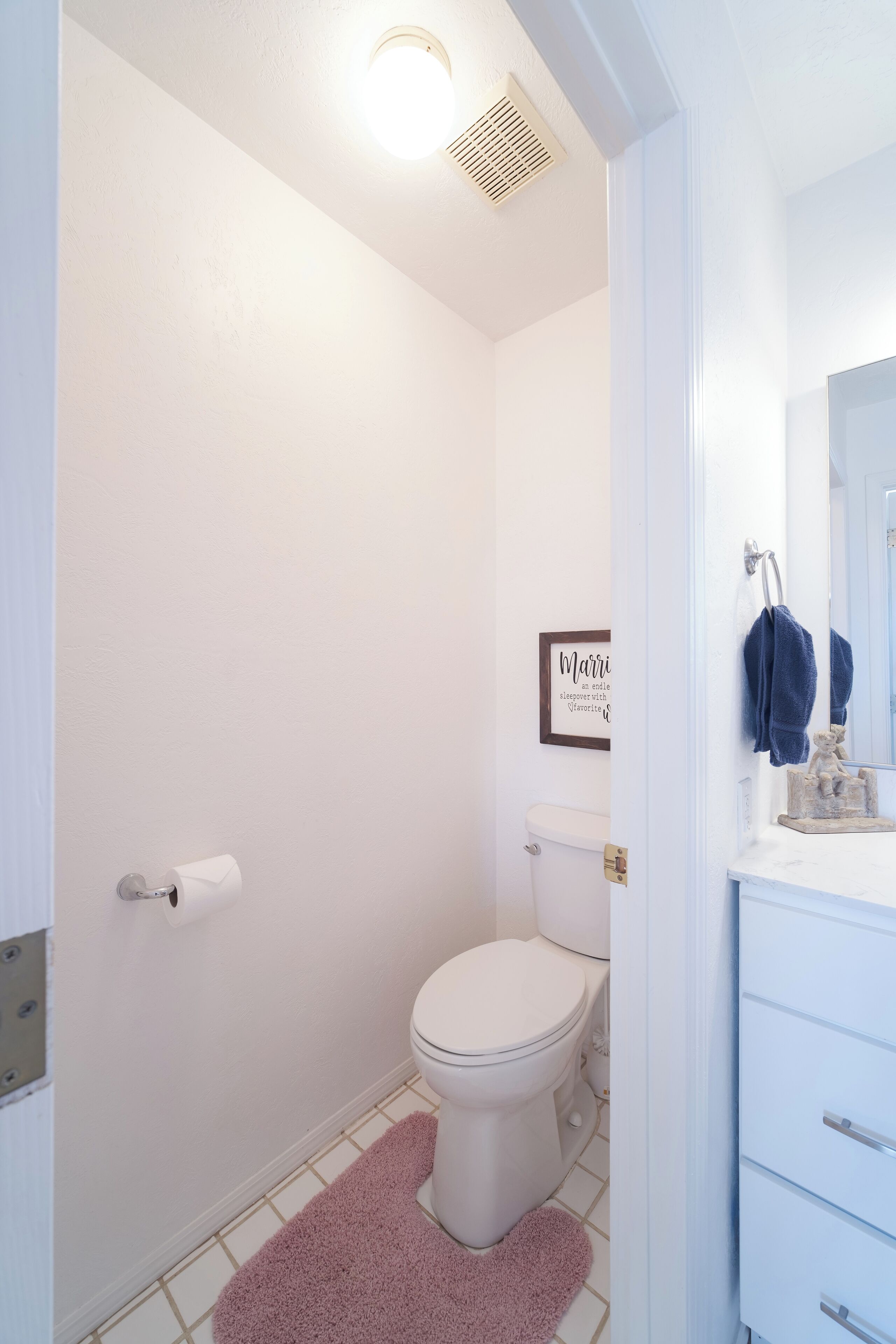 A bathroom with a toilet, a sink, a mirror, and a framed sign on the wall.