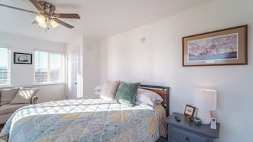 Un dormitorio con cama, mesita de noche, ventilador de techo, un cuadro en la pared y ventana con persianas.