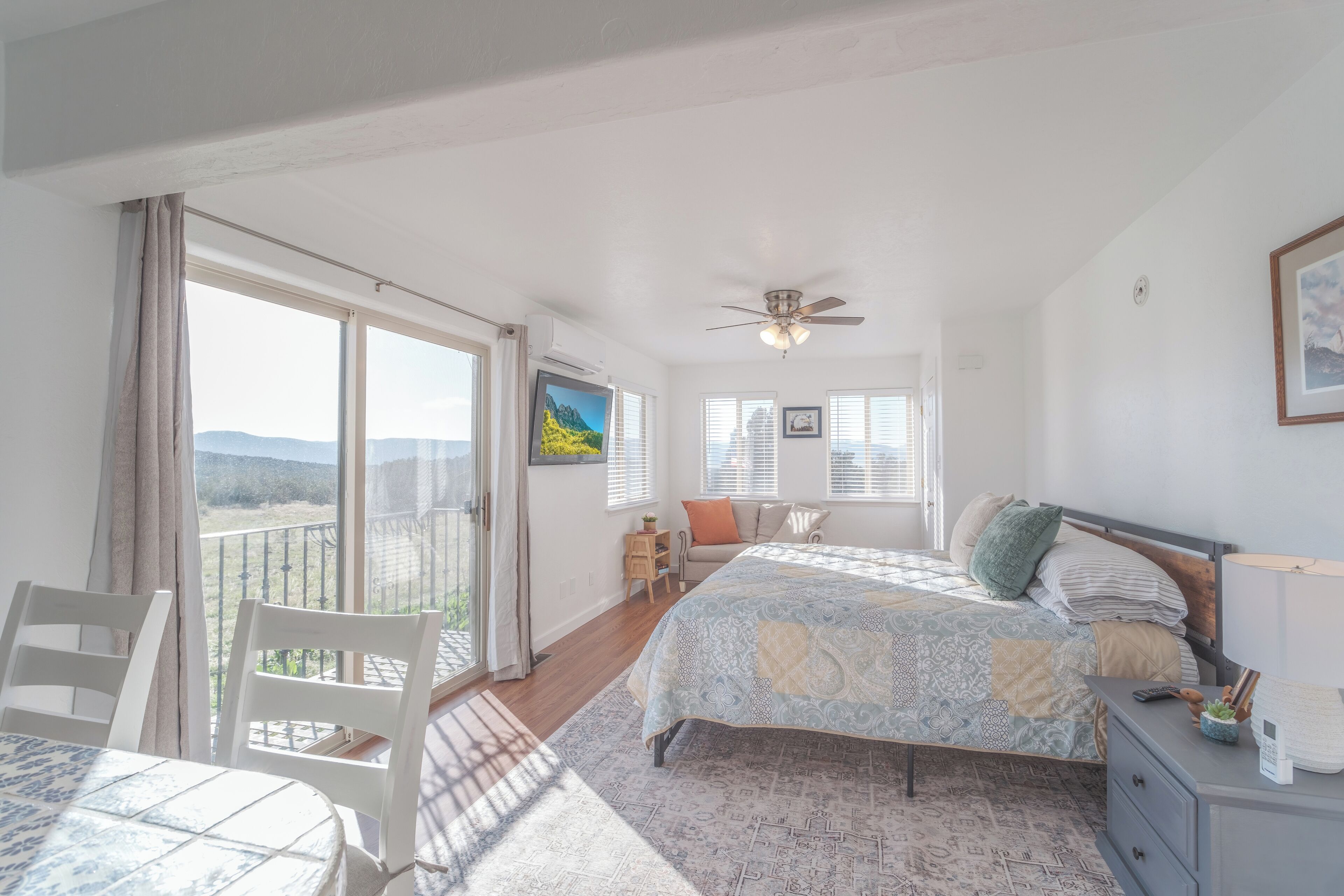 A bedroom with a bed, a desk, a chair, a balcony, and a ceiling fan.