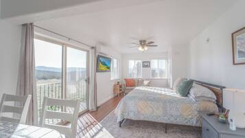 A bedroom with a bed, a desk, a chair, a balcony, and a ceiling fan.