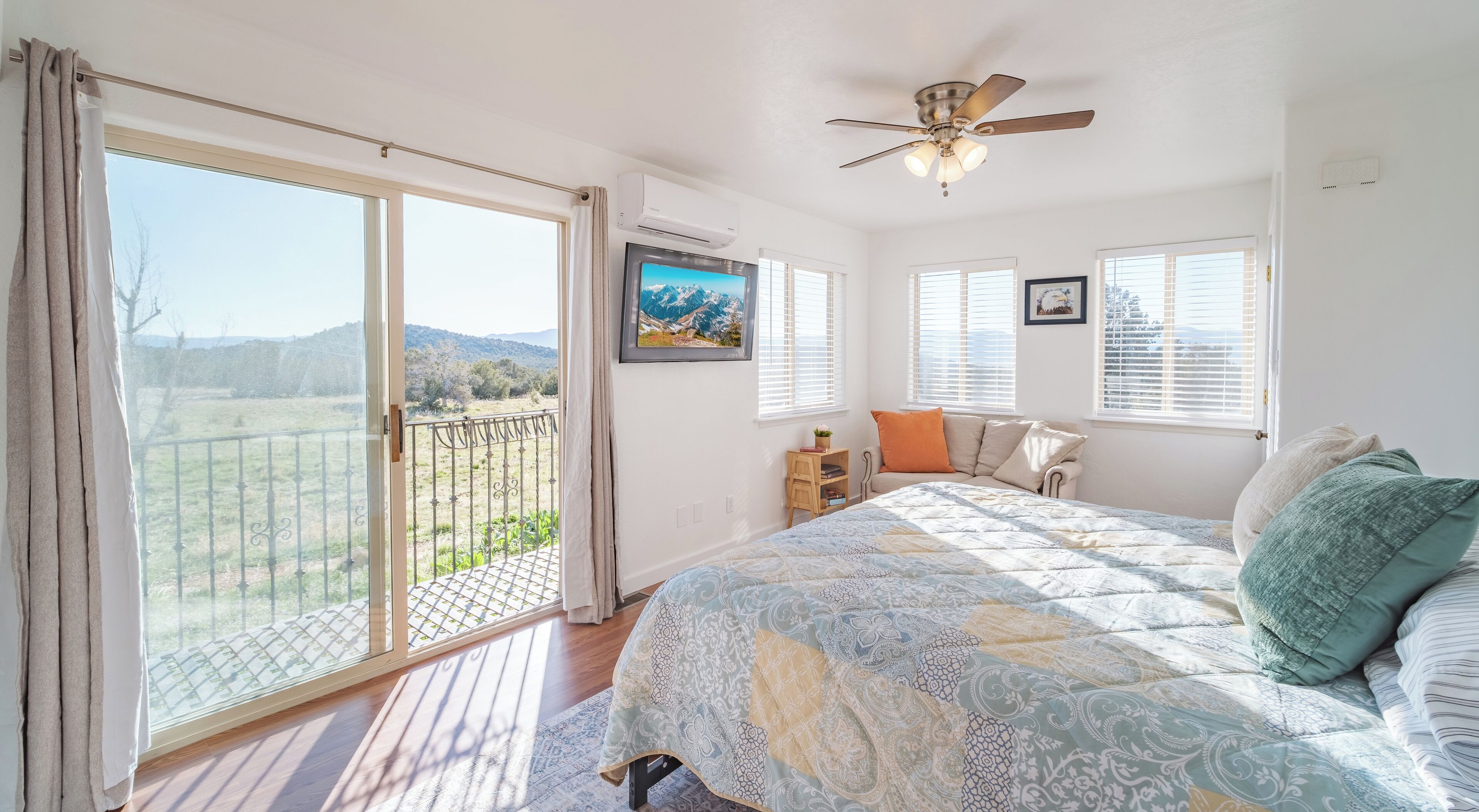 A bedroom with a large bed, a ceiling fan, a TV, and a view of a balcony.