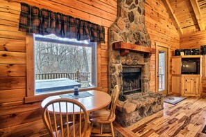 A cozy cabin interior with a stone fireplace, wooden walls, a dining table with chairs, and a large window overlooking a snowy deck. - Grant's Escape - Couples Cabin in Hocking Hills (Logan)