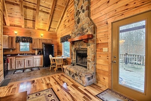 A log cabin interior with a stone fireplace, wooden floors, and a view of the deck. - Grant's Escape - Couples Cabin in Hocking Hills (Logan)