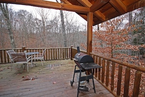 A wooden deck with a grill, chairs, and a table.