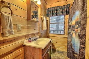 A wooden cabin bathroom with a sink, mirror, towel rack, and window with a view of a snowy landscape.