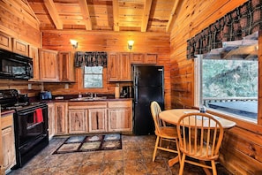 A cozy cabin-style kitchen with wooden walls and ceiling, a black refrigerator, a stove, and a dining table with chairs. - Grant's Escape - Couples Cabin in Hocking Hills (Logan)