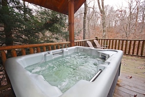A hot tub on a wooden deck with a view of trees.