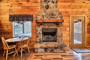 A stone fireplace with a mantel, wooden walls, a dining table with chairs, and a door with a view of a balcony. - Grant's Escape - Couples Cabin in Hocking Hills (Logan)