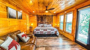 A log cabin room with a bed, a leather couch, and large windows. - Summer Deals/Amazing Views/Dollywood/Pet Friendly (Sevierville)