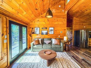 A cozy cabin interior with a wooden ceiling, a sofa with cushions, a coffee table, and a refrigerator. - Fall Deals/Amazing Views/Dollywood/Pet Friendly (Sevierville)