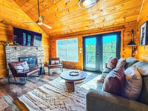Ein gemütliches Blockhaus-Interieur mit Kamin, Ledermöbeln und einem großen Fenster.