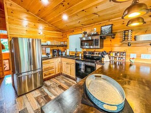 Interior de una cabaña de madera con cocina, que incluye un refrigerador de acero inoxidable, un microondas y una estufa.