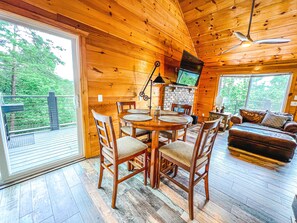 Relax in a cozy cabin-style retreat with a dining area, comfortable seating, and a large window offering a view of the surrounding greenery.