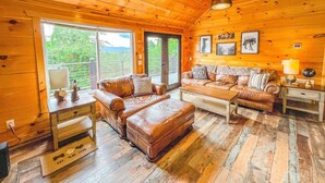 A wooden cabin interior with leather sofas, a ceiling fan, and large windows. - Summer Deals/Amazing Views/Dollywood/Pet Friendly (Sevierville)